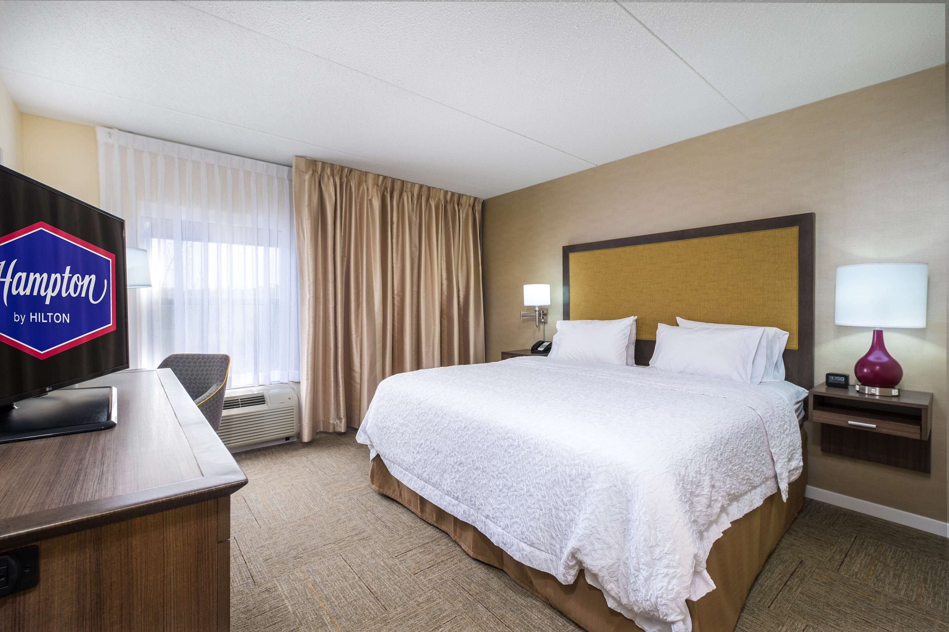 A hotel room with a large bed, a desk with a computer, a TV, and a lamp.