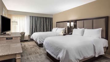 A hotel room with two beds, a desk, a TV, and a lamp.
