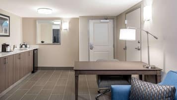 A hotel room with a kitchenette, a dining table, a sofa, and a desk.