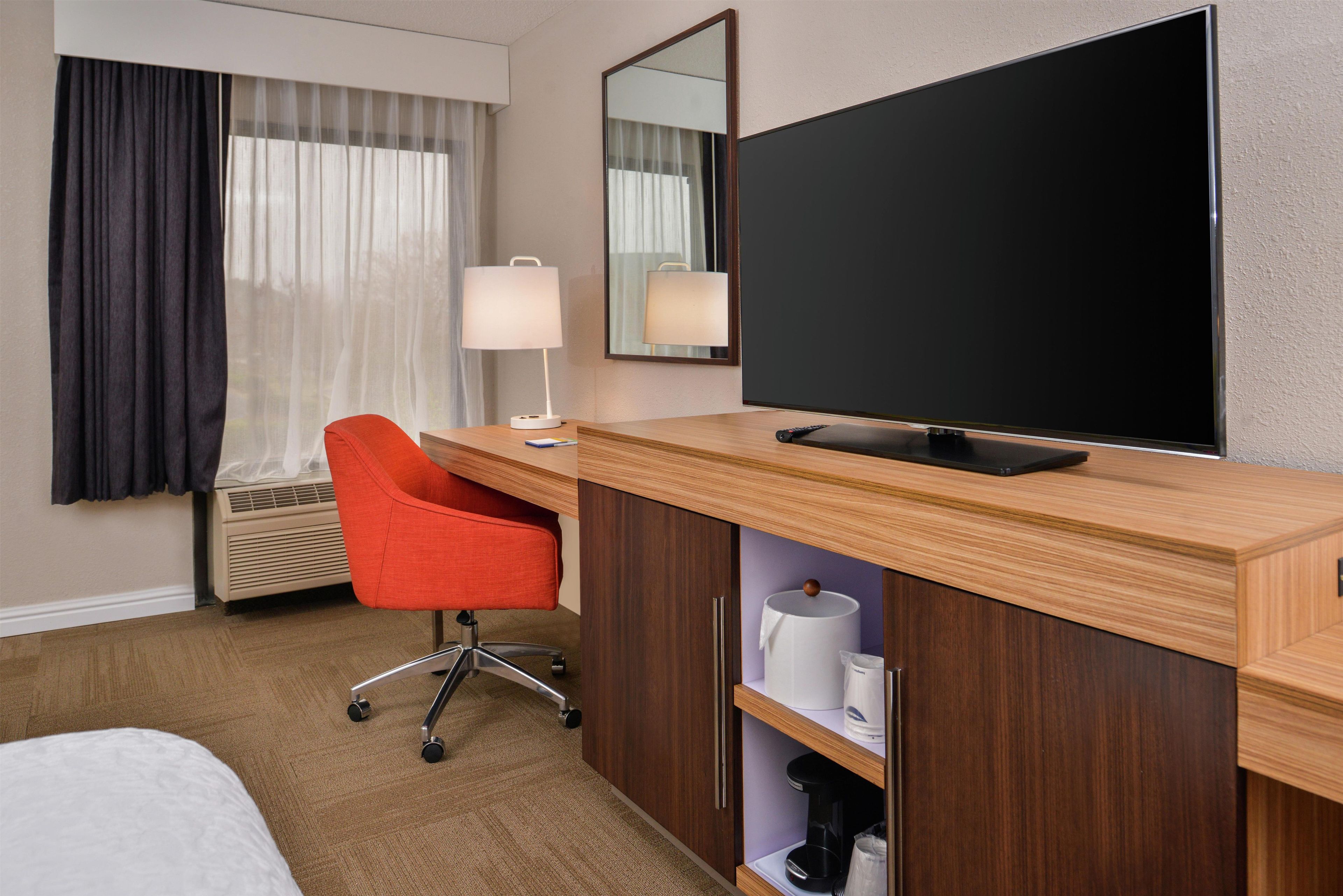 A hotel room with a bed, a desk with a chair, a television, and a window with curtains.
