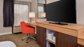 A hotel room with a bed, a desk with a chair, a television, and a window with curtains.