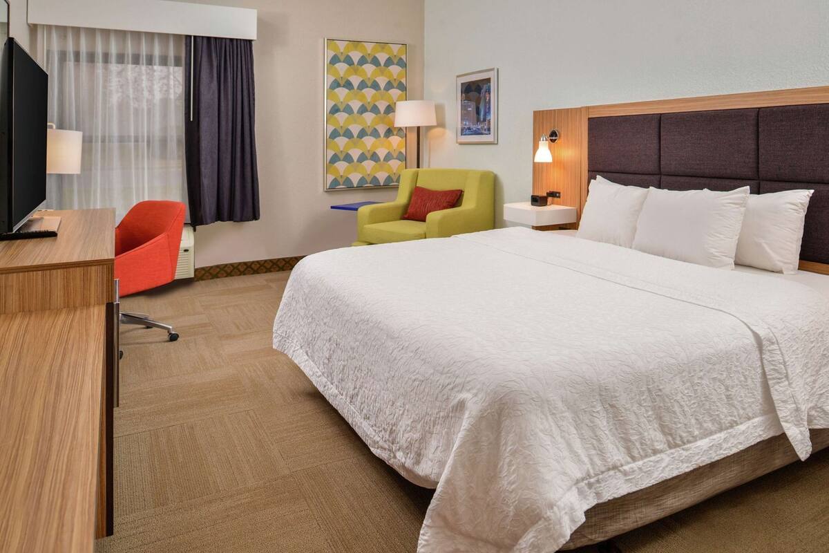 Ein Hotelzimmer mit Bett, Schreibtisch, Stuhl, Lampe und einem Bild an der Wand.