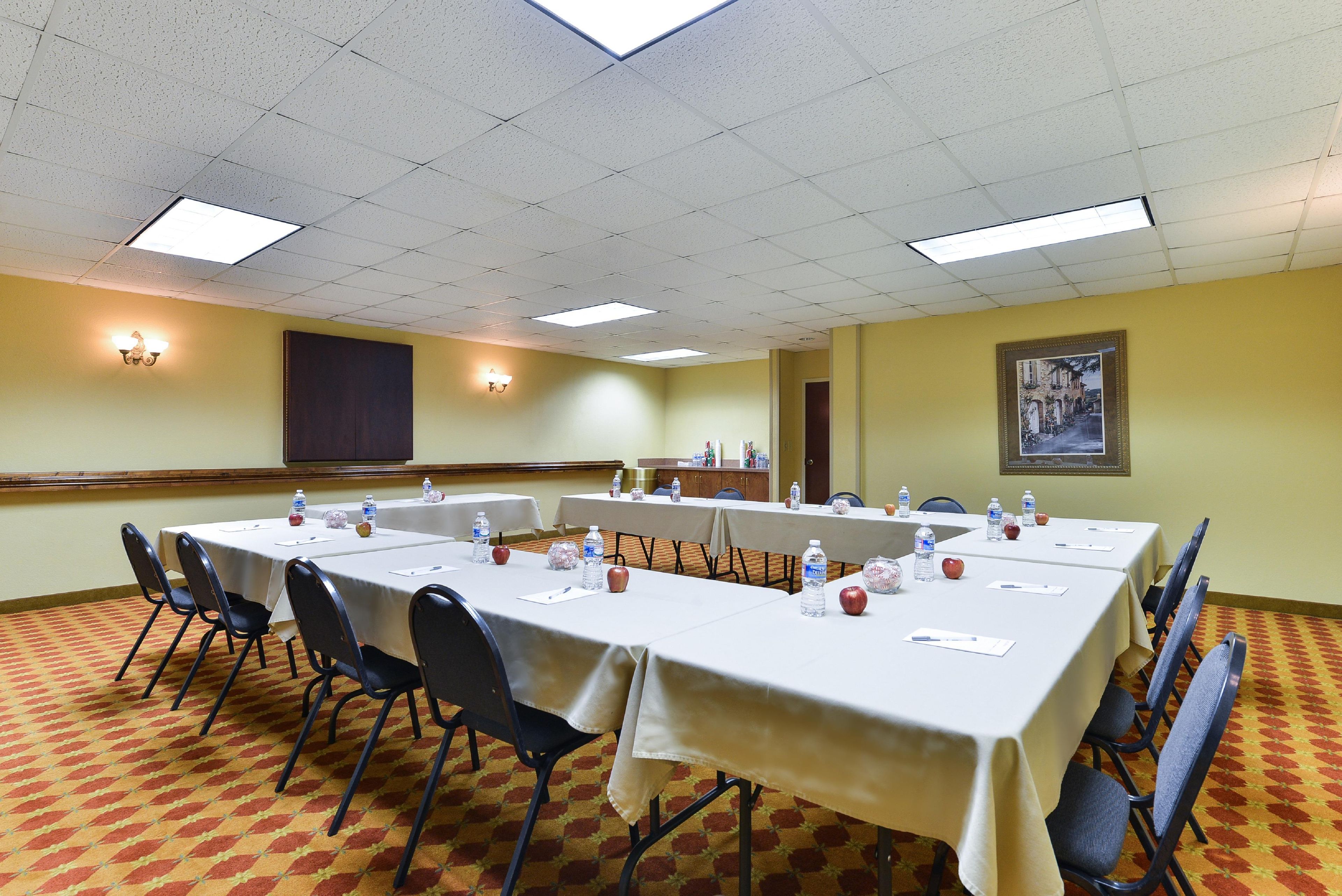 A conference room with tables set for meetings, equipped with water bottles and apples, and a large painting on the wall.