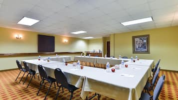 A conference room with tables set for meetings, equipped with water bottles and apples, and a large painting on the wall.