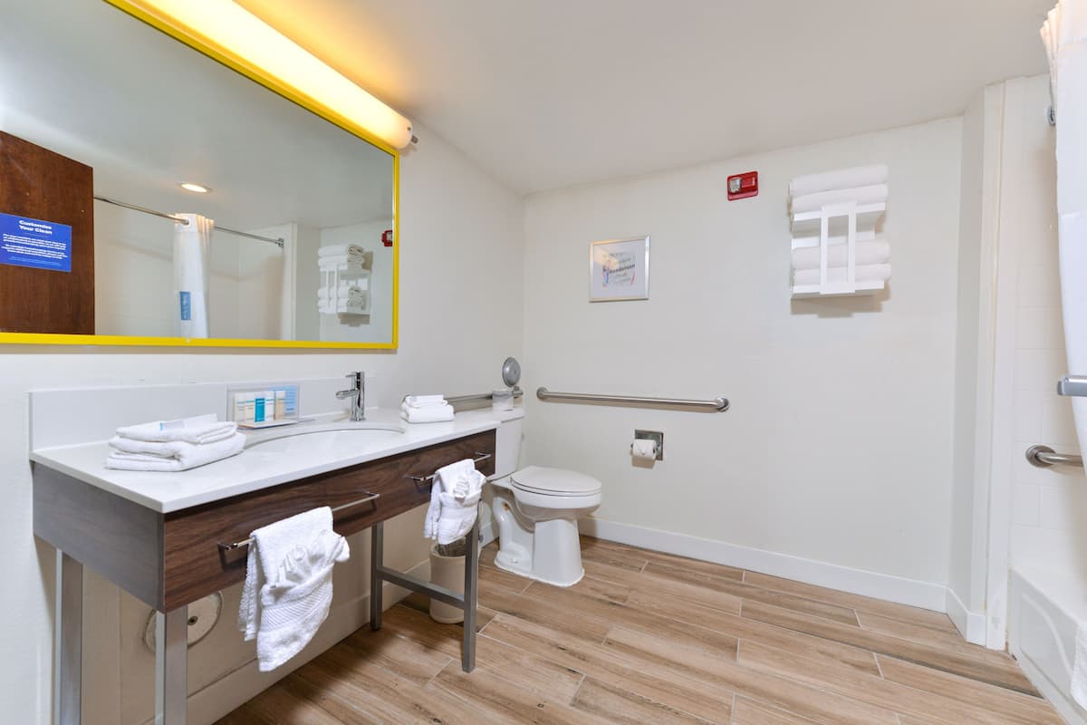A bathroom with a sink, mirror, toilet, and a handrail.