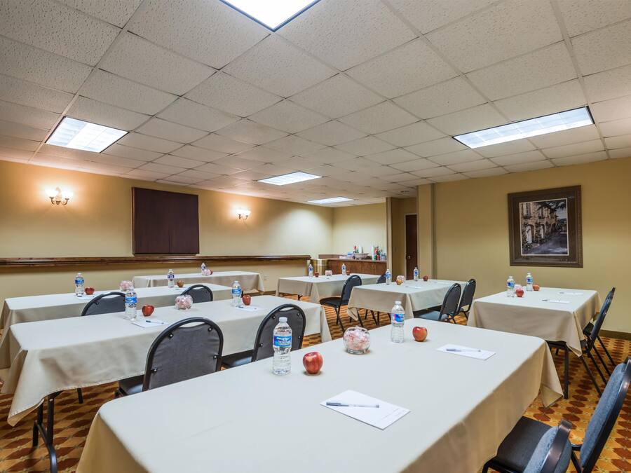 Un salón de conferencias con varias mesas, sillas, botellas de agua, manzanas y un cuadro en la pared.