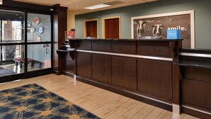 A hotel reception area with a wooden reception desk, a glass door entrance, and a framed picture on the wall. - Hampton Inn Raleigh/Clayton I-40 (Garner)