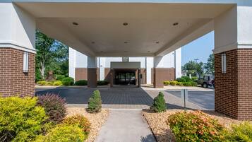 A building entrance with a covered walkway, brick walls, and a parking area with vehicles.