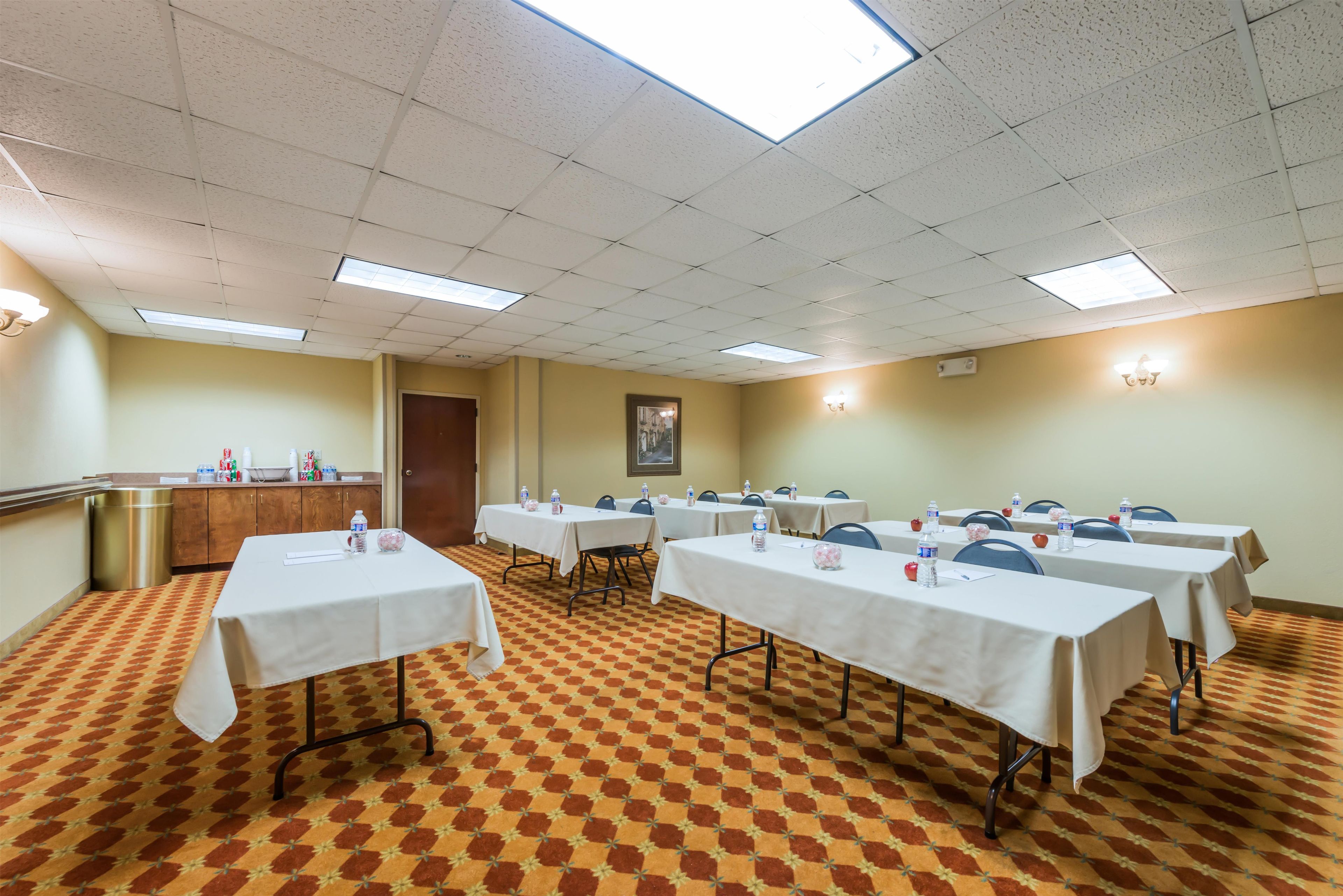 A conference room with multiple tables, chairs, and a patterned carpet.