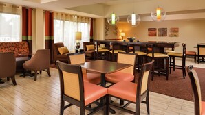 A hotel dining area with multiple tables and chairs, a sofa, and decorative wall art. - Hampton Inn Raleigh/Clayton I-40 (Garner)