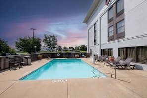 A swimming pool with lounge chairs and a deck area, surrounded by a building with large windows.