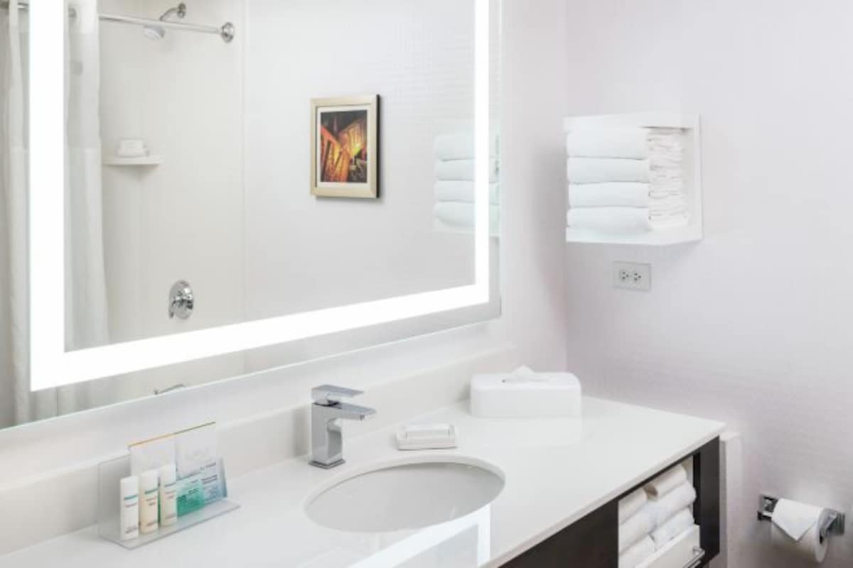 A hotel bathroom with a large mirror, a sink, a towel rack, and a towel dispenser.