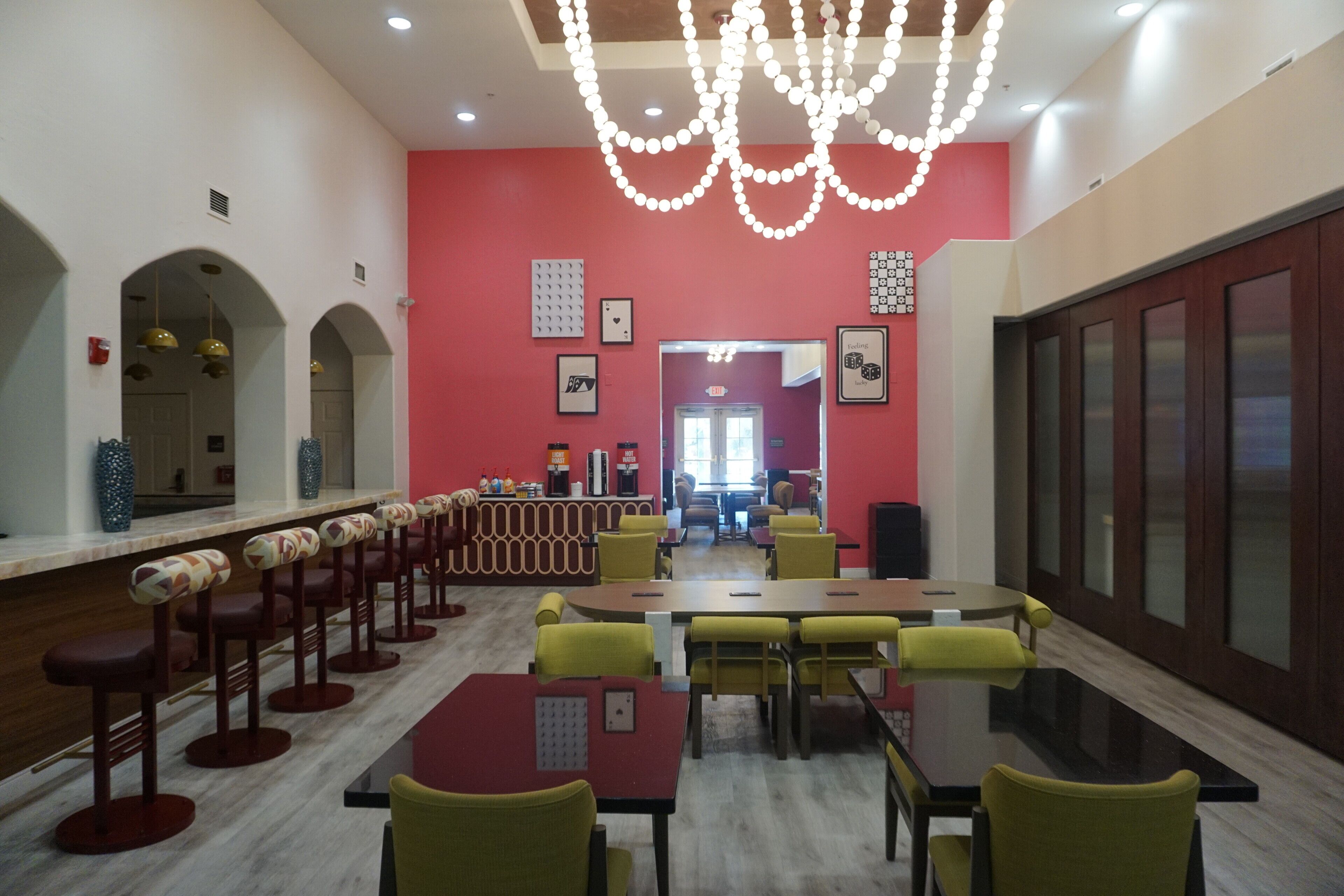 A modern dining area with a long counter, multiple bar stools, and yellow chairs.