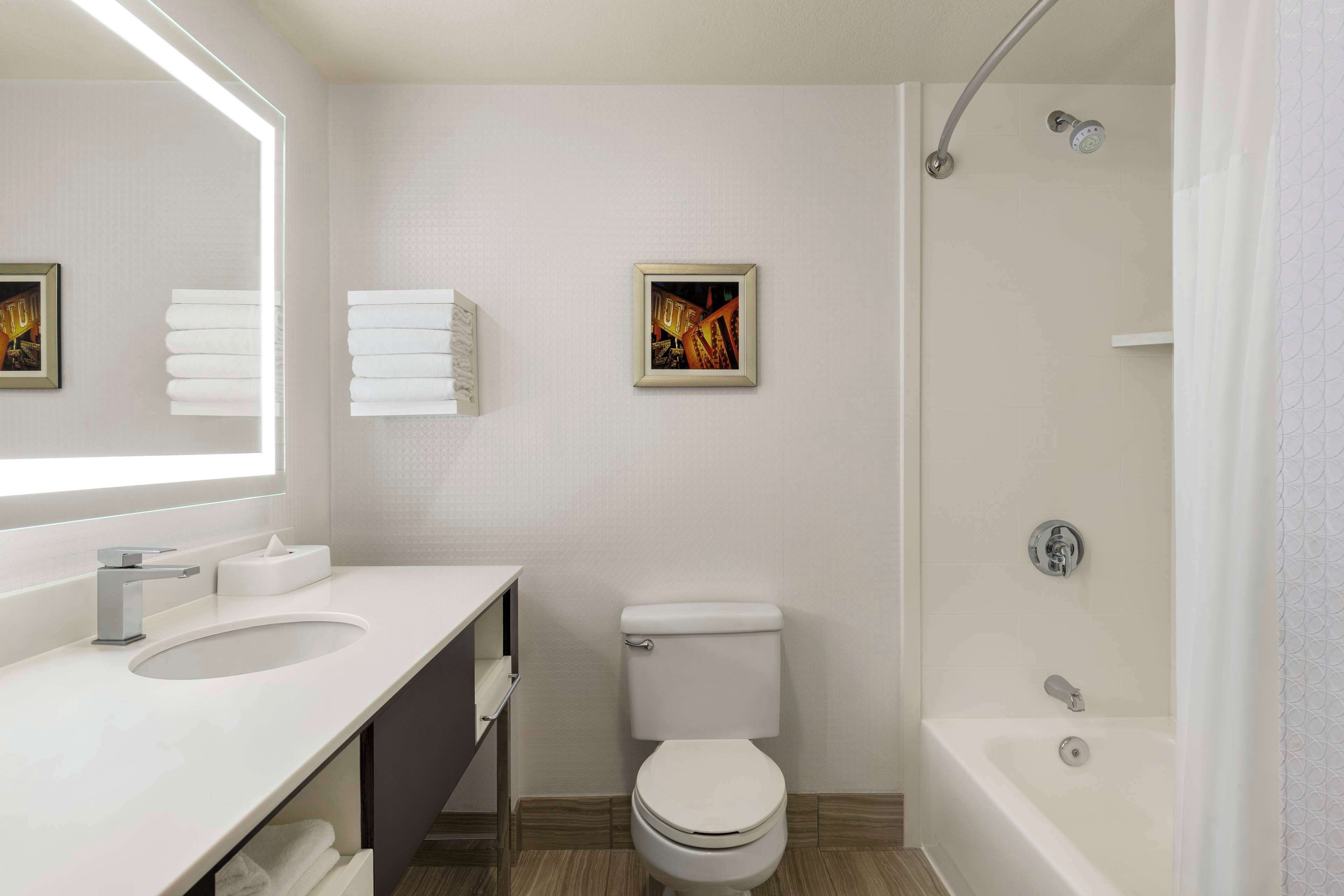A modern bathroom with a white sink, toilet, and bathtub. There is a framed picture on the wall and a towel rack.