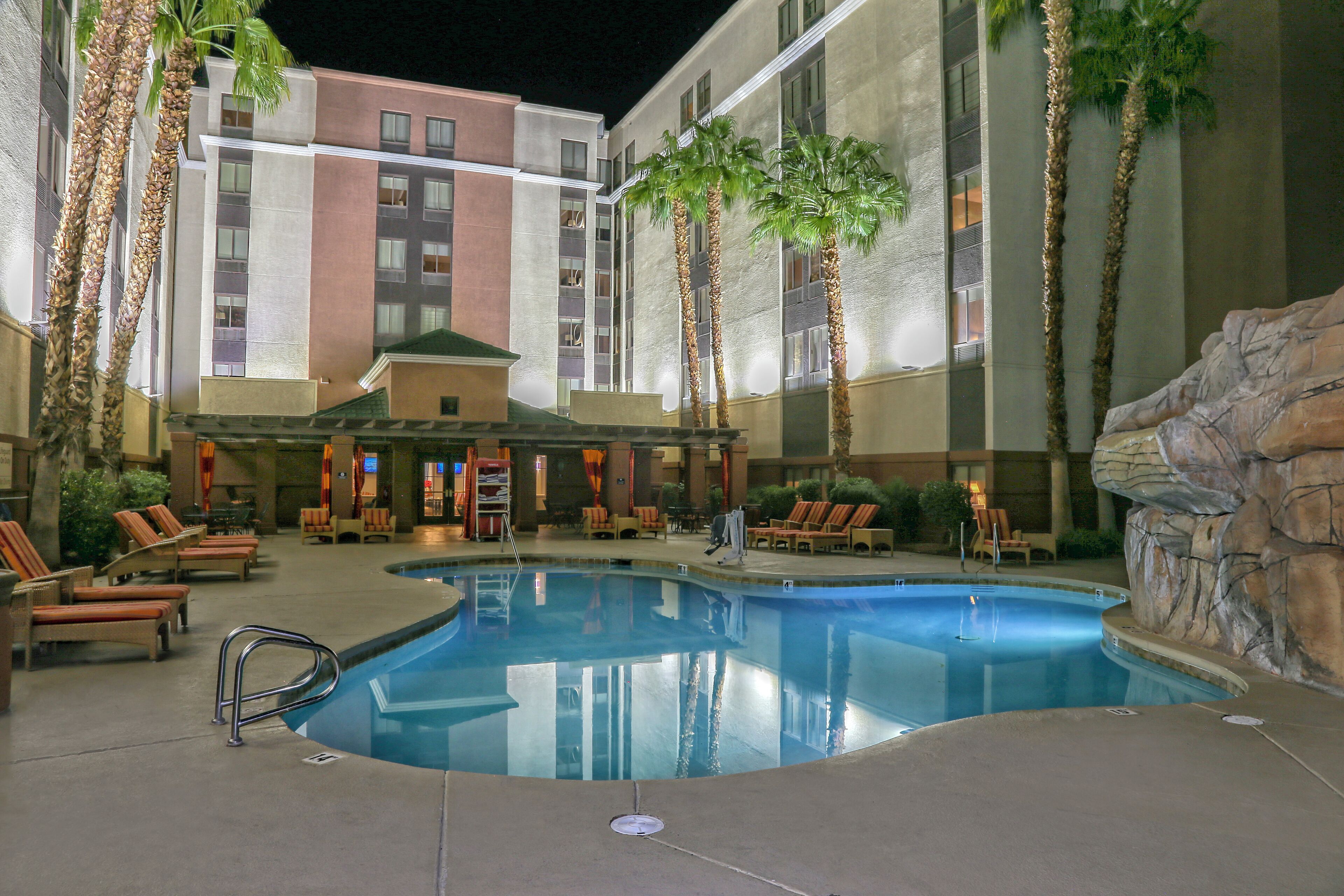 A hotel pool area with lounge chairs and palm trees.