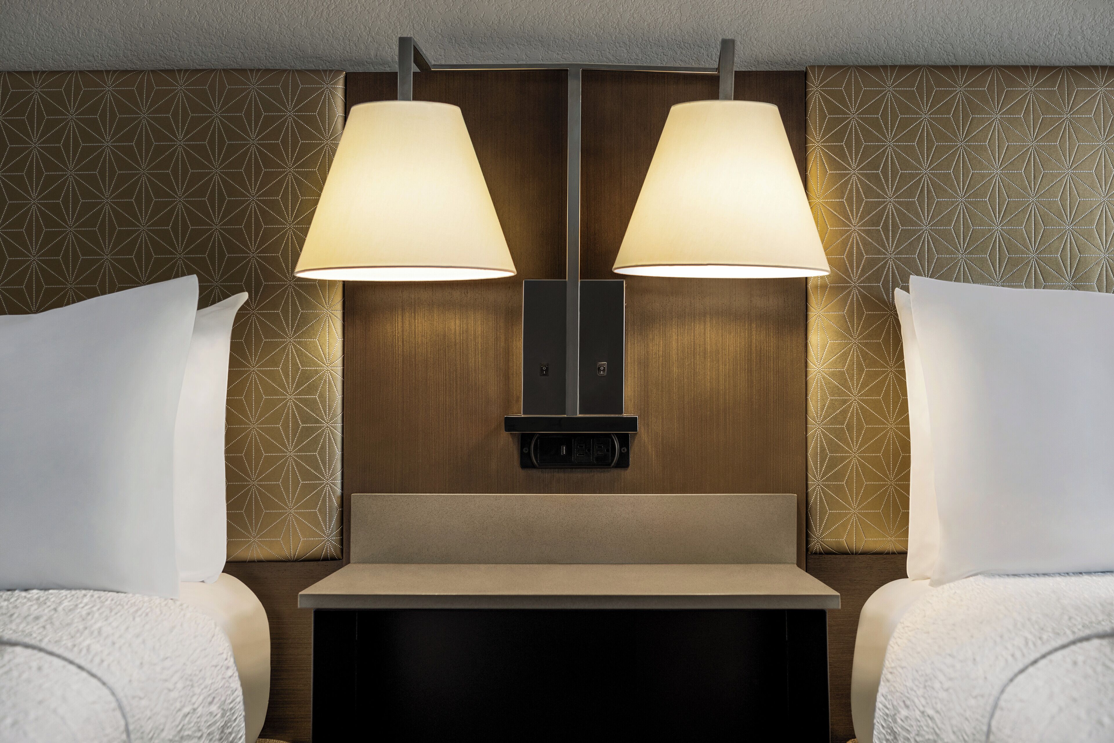 Une chambre d’hôtel avec un lit, deux lampes de chevet, un panneau de commande et un papier peint à motifs.