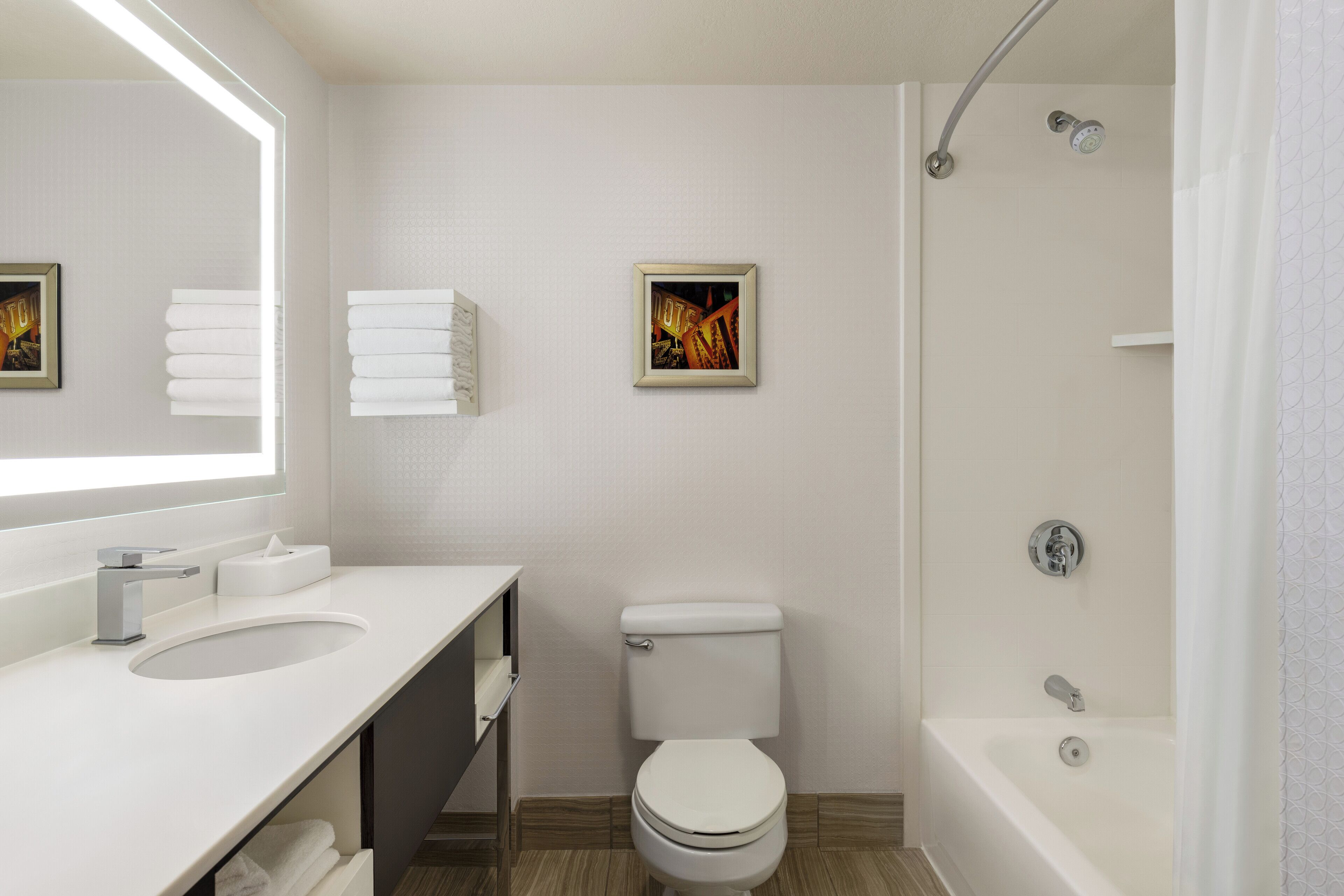 Ein modernes Badezimmer mit einem weißen Waschbecken, einer Toilette und einer Badewanne. An der Wand hängt ein gerahmtes Bild und es gibt einen Handtuchhalter.