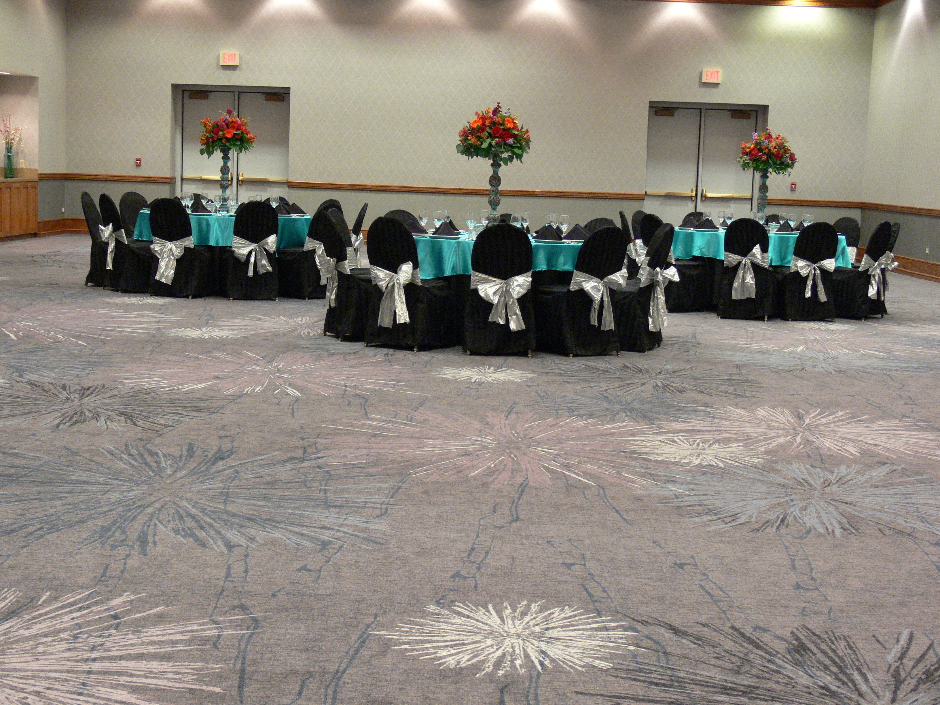 A conference room with tables set for a meeting, chairs with silver sashes, and floral centerpieces.