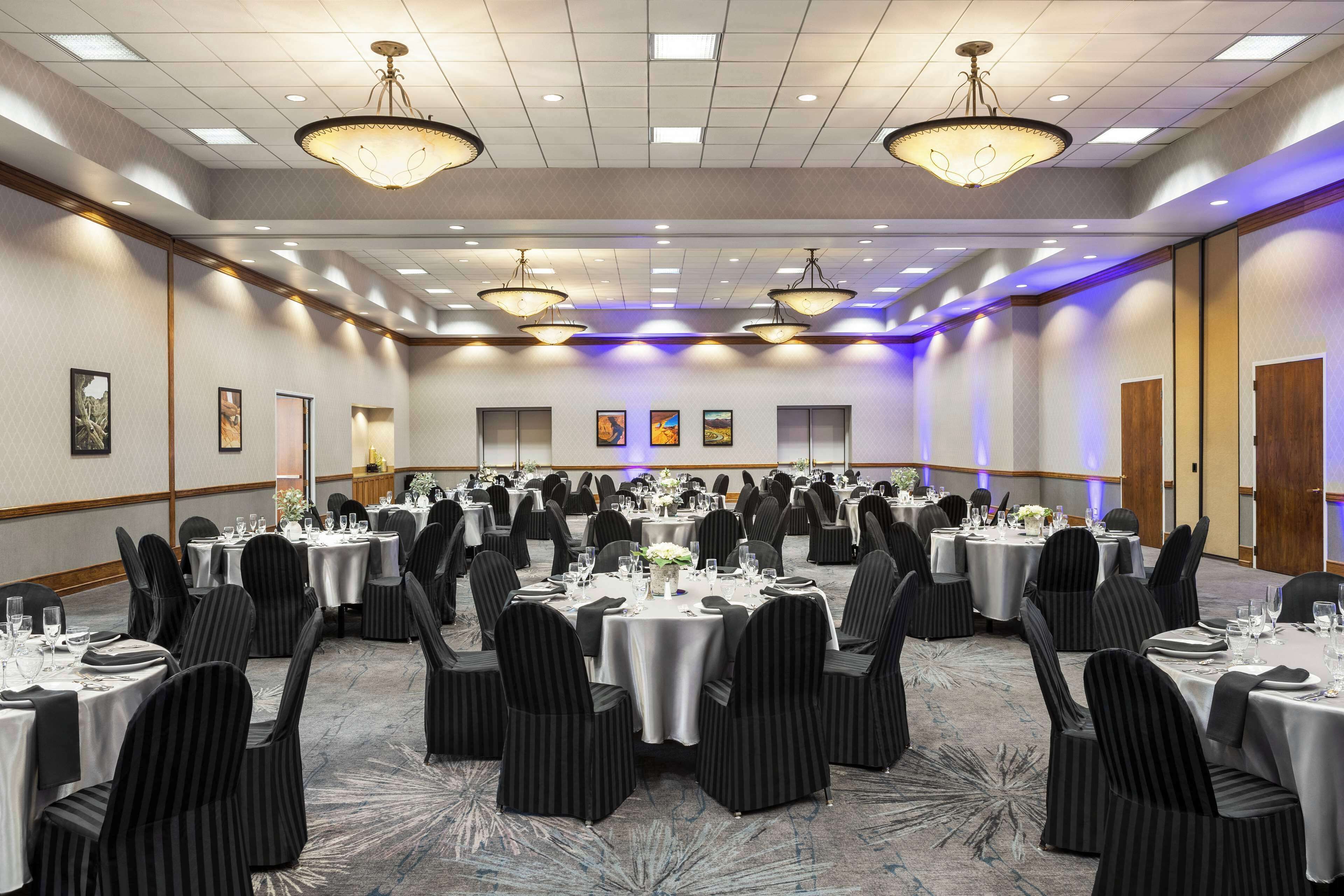Un amplio salón de conferencias con mesas y sillas redondas, equipado con mantelería y un candelabro.