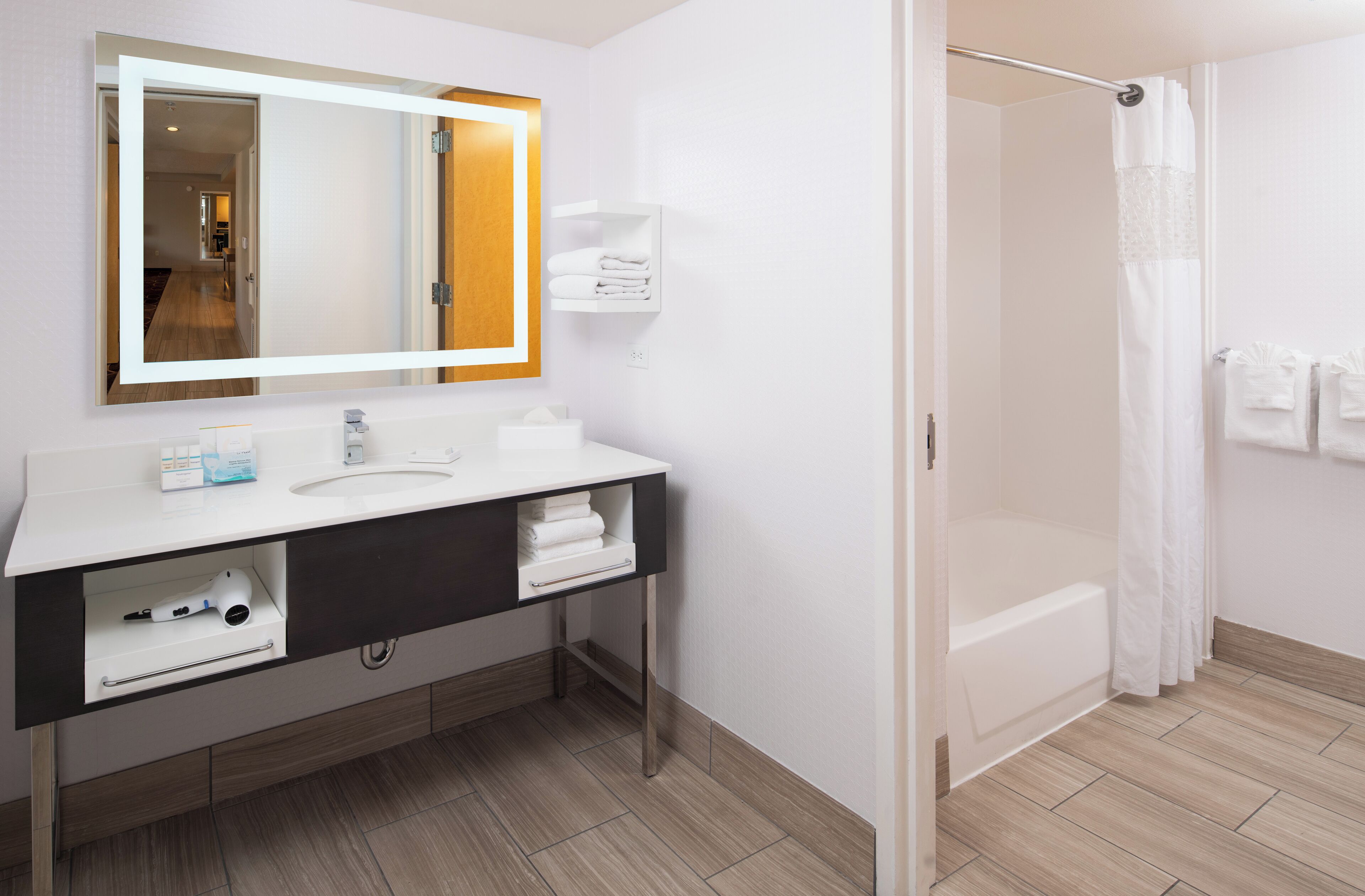Un baño moderno con un tocador blanco, un espejo grande, una bañera y una cortina de ducha.