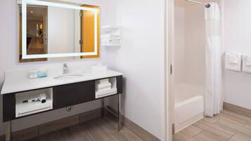 Un baño moderno con un tocador blanco, un espejo grande, una bañera y una cortina de ducha.