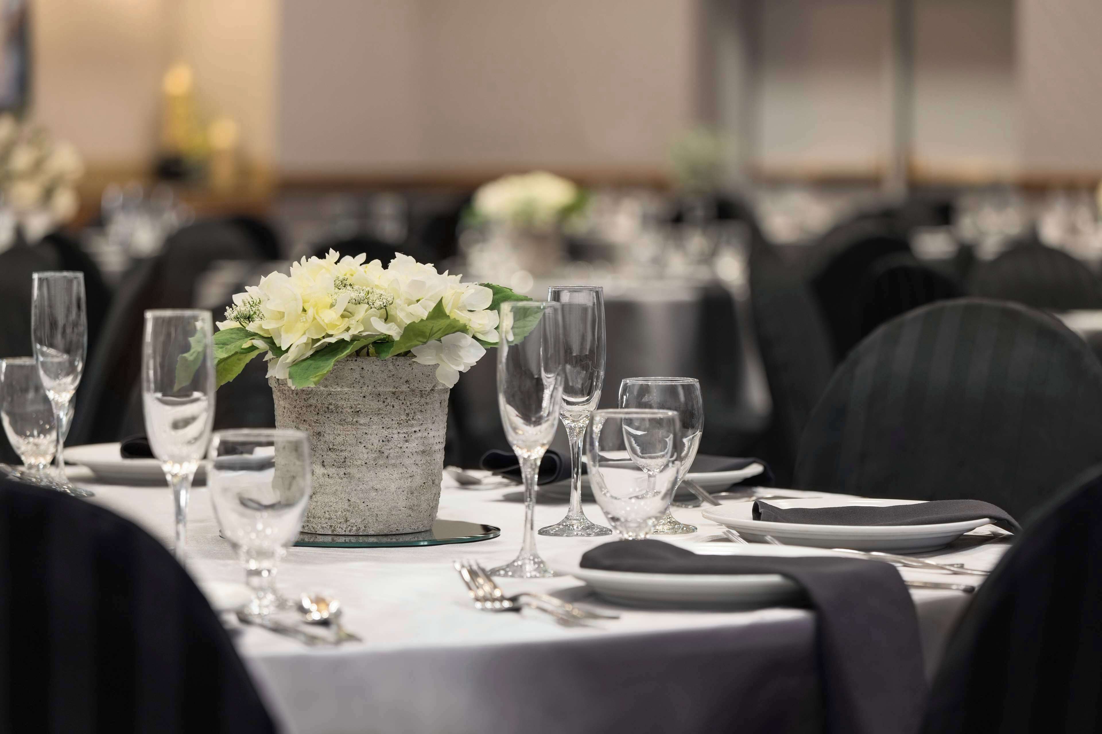 A dining table set with white flowers, clear glasses, and cutlery.