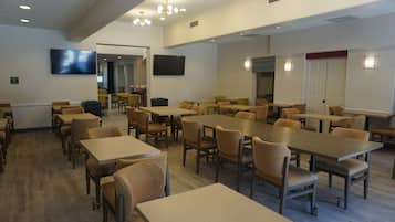 Un grand espace dédié à la salle à manger, avec plusieurs tables et chaises, un téléviseur fixé au mur et une porte dont l’encadrement est de couleur rouge.
