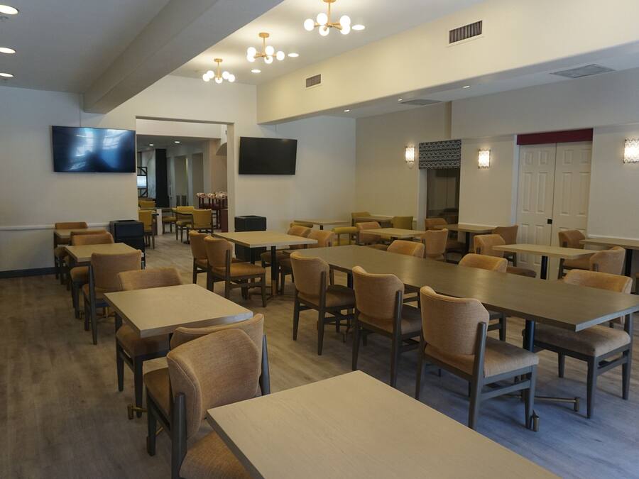 Un grand espace dédié à la salle à manger, avec plusieurs tables et chaises, un téléviseur fixé au mur et une porte dont l’encadrement est de couleur rouge.