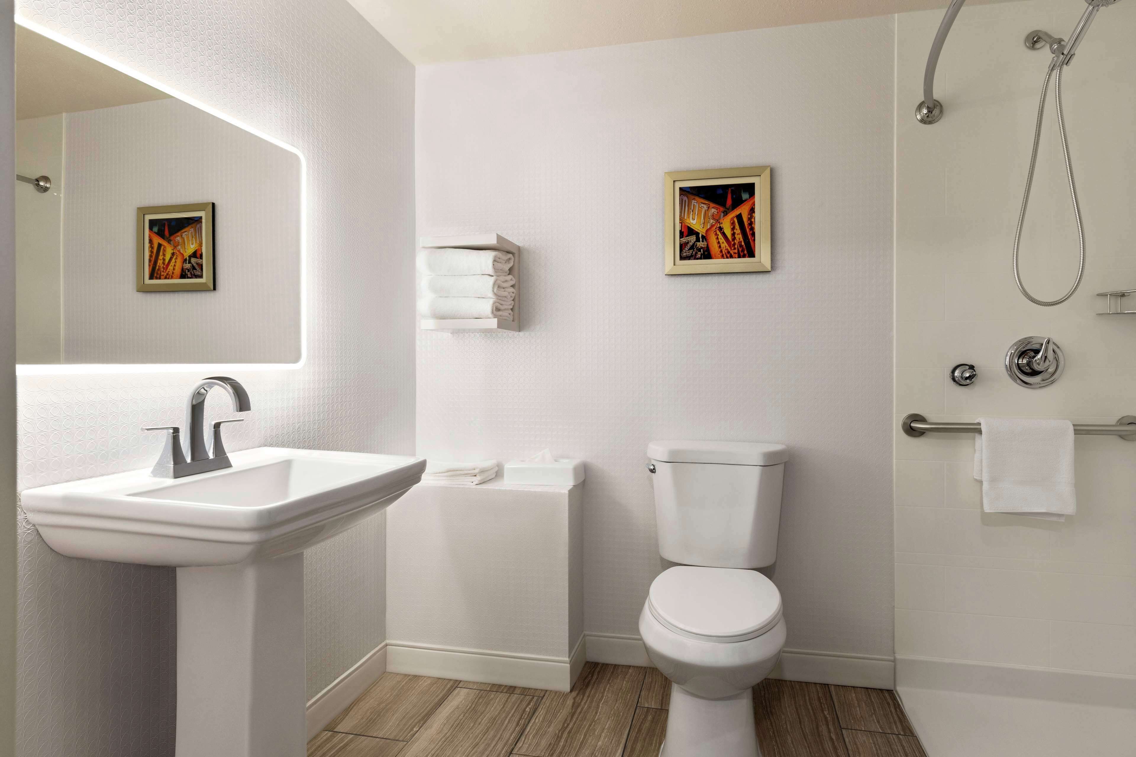 Une salle de bain avec un lavabo, des toilettes et une douche. Deux tableaux encadrés sont accrochés au mur.
