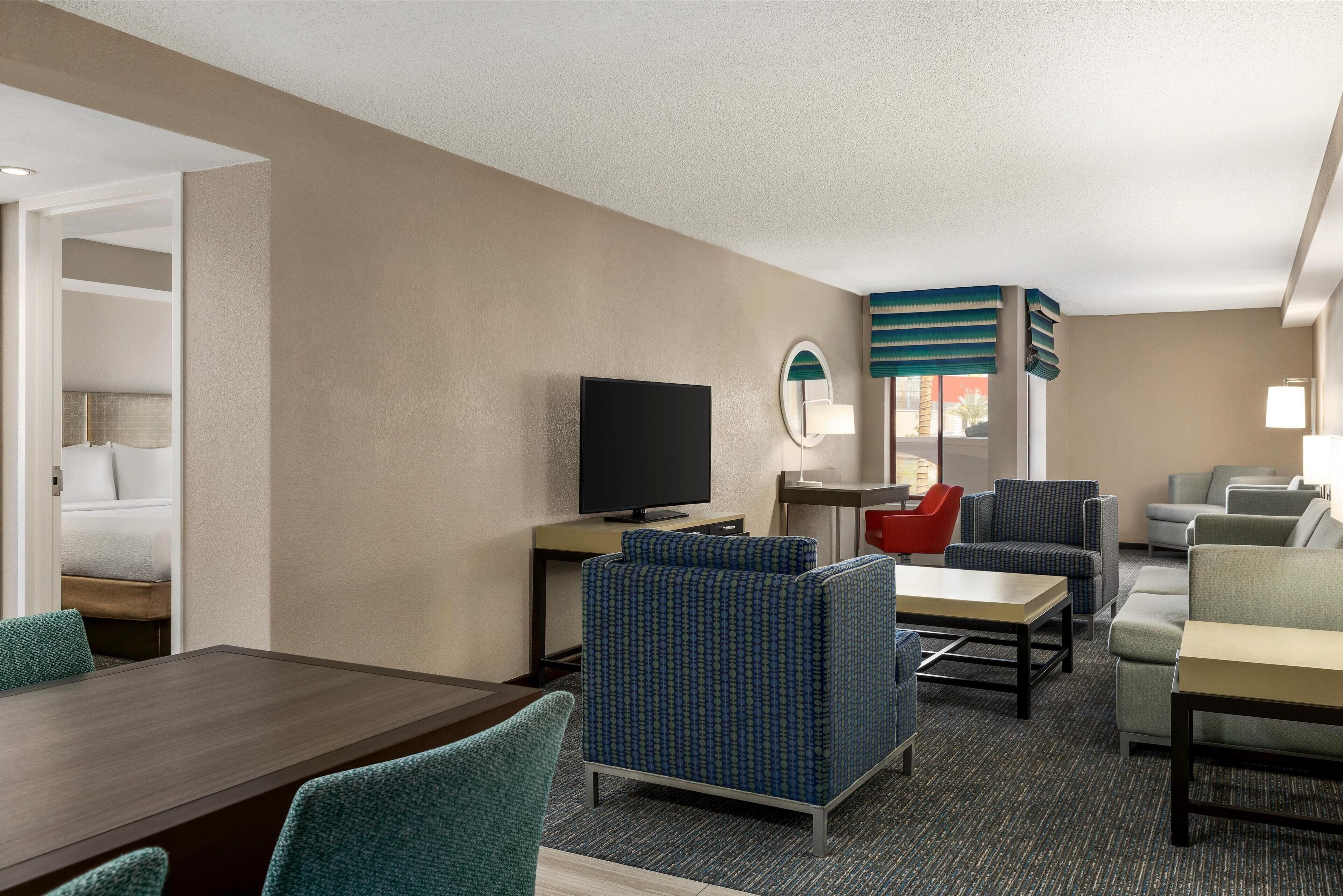 A hotel room with a dining area, a TV, and seating arrangements.