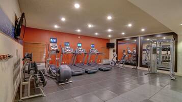 Ein Fitnessstudio mit Laufbändern, Krafttrainingsgeräten und einer Spiegelwand.