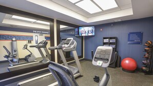 A fitness center with treadmills, an elliptical, a stationary bike, a red exercise ball, and a television displaying a show.
