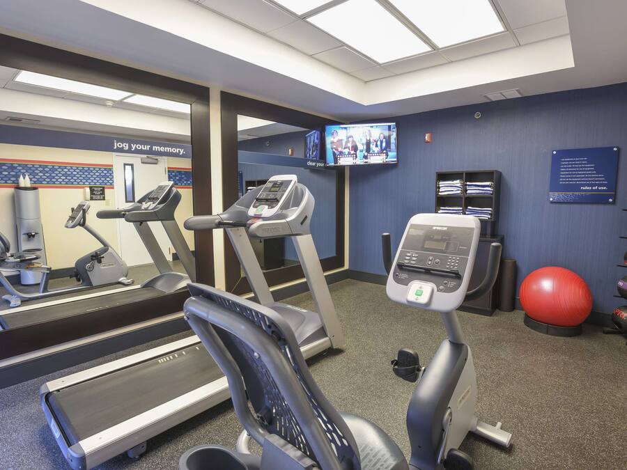 A fitness center with treadmills, an elliptical, a stationary bike, a red exercise ball, and a television displaying a show.