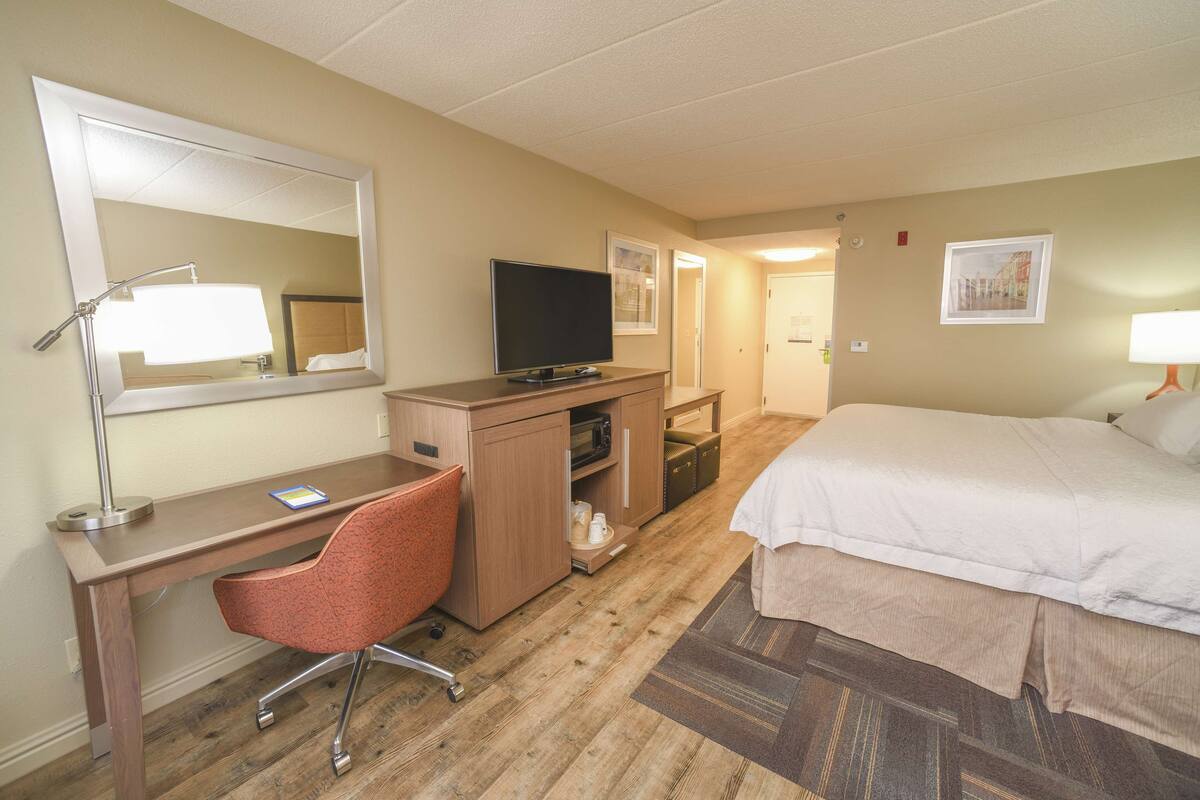 Ein Hotelzimmer mit Bett, Schreibtisch, Stuhl, Fernseher und Spiegel.