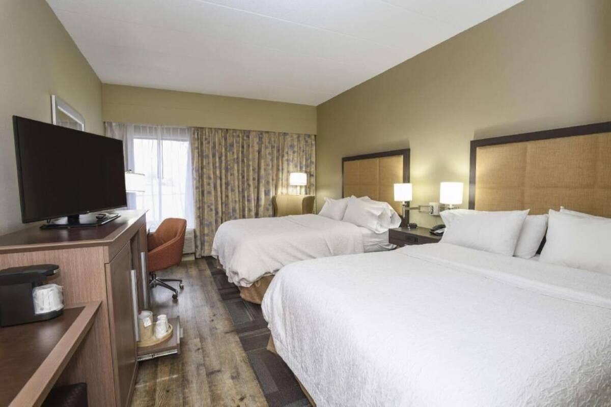 Ein Hotelzimmer mit zwei Betten, einem Schreibtisch mit Fernseher, einer Kaffeemaschine und einem Sessel.