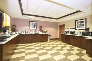 A hotel kitchen with checkered flooring, wooden cabinets, and various coffee-making equipment.