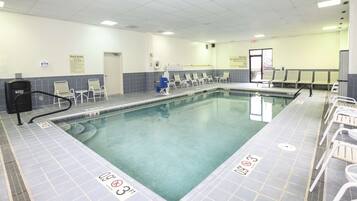 Piscina com deck ladrilhado, espreguiçadeiras e cadeira do salva-vidas.
