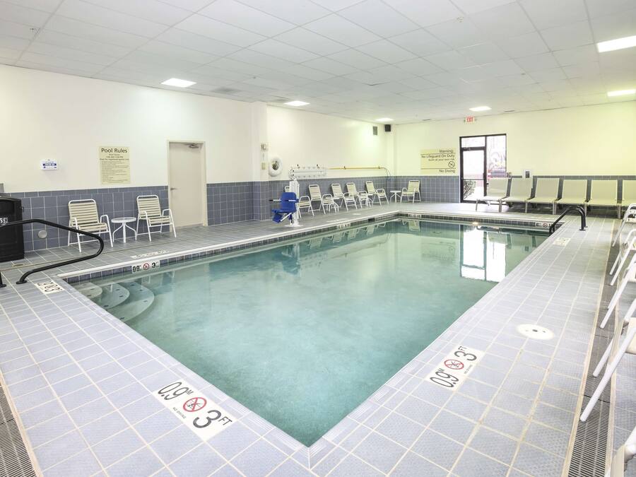 Piscina com deck ladrilhado, espreguiçadeiras e cadeira do salva-vidas.