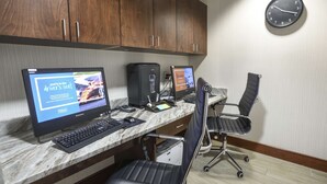 A hotel room with a marble desk, two computers, a chair, and a clock on the wall.