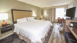 A hotel room with a large bed, a desk with a television, a chair, and a lamp.