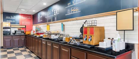 Un espace cuisine moderne avec un carrelage à motifs, un long comptoir doté de divers appareils et un mur noir où sont écrits les plats à la carte.