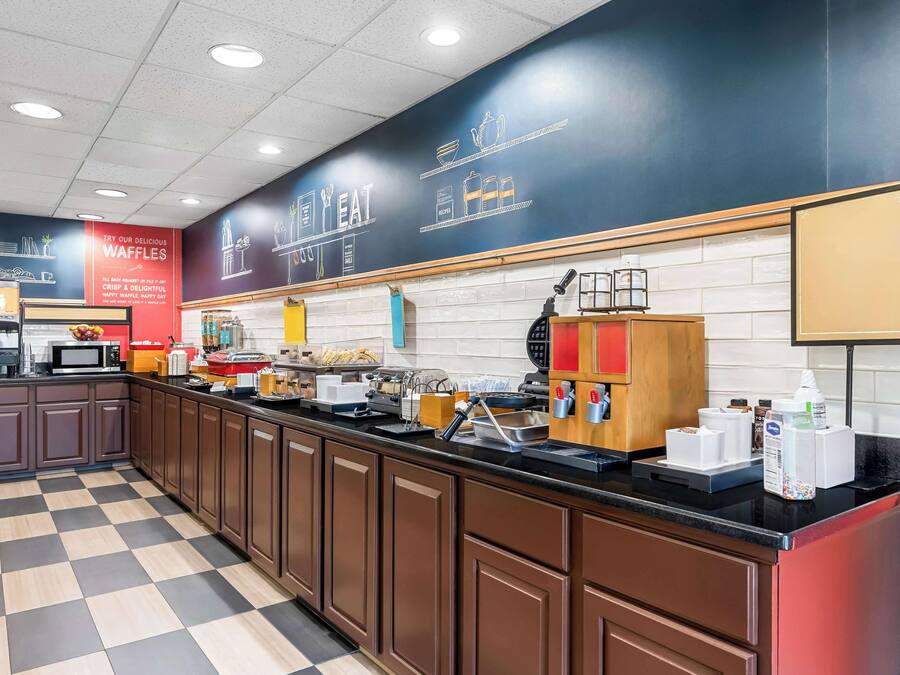A modern kitchen area with a checkered floor, a long counter with various appliances, and a chalkboard wall with menu items.