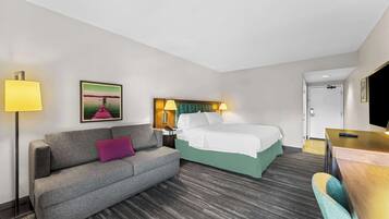 Quarto de hotel com cama, sofá, escrivaninha e televisão.