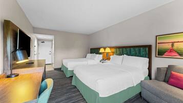 A hotel room with two beds, a desk with a lamp, a chair, a sofa, and a painting on the wall.