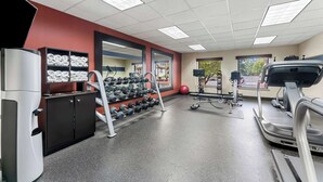 Ein Fitnessraum mit Laufbändern, Kurzhanteln und einer Gewichtshebench.