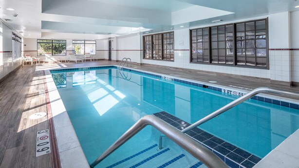 Piscina interna com água cristalina, paredes revestidas de azulejos e piso de madeira.