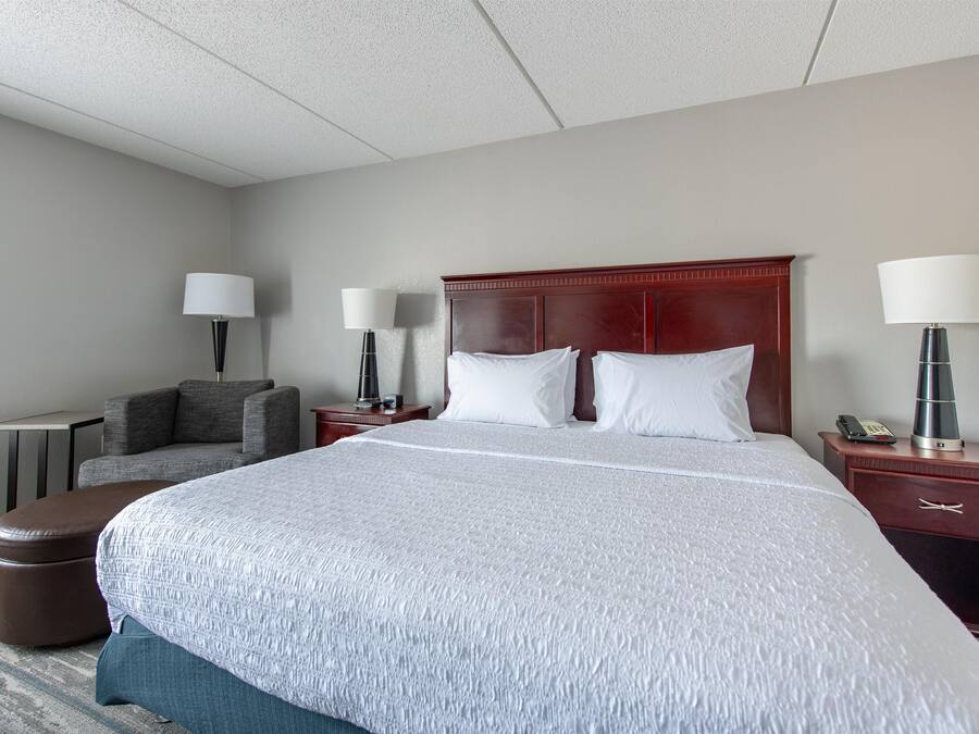 Habitación de hotel con una cama grande, dos mesitas de noche, una silla y dos lámparas.