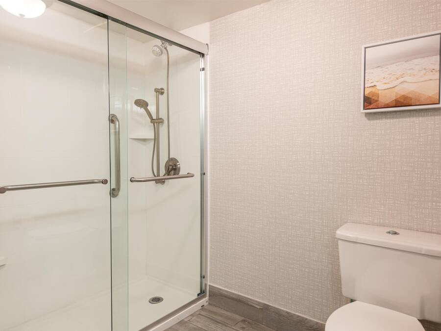 Ein Badezimmer mit einer Duschkabine aus Glas, einer Toilette und einem gerahmten Bild an der Wand.