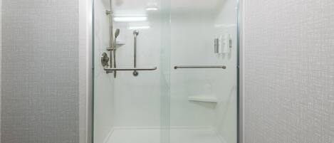 A glass-enclosed shower stall with a handrail, a showerhead, and a control panel.
