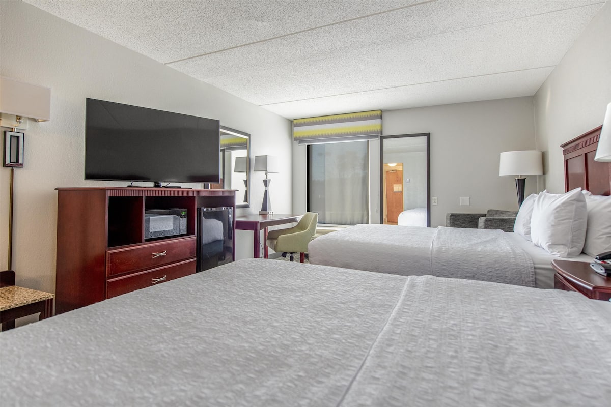 Une chambre d’hôtel avec deux lits, une télévision, un bureau avec une lampe et une chaise.